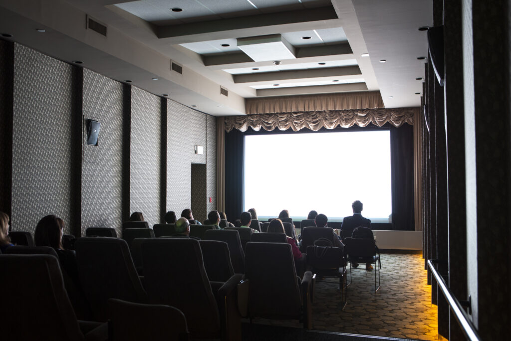 People in a small theater watching a projected screen at the front of the room.