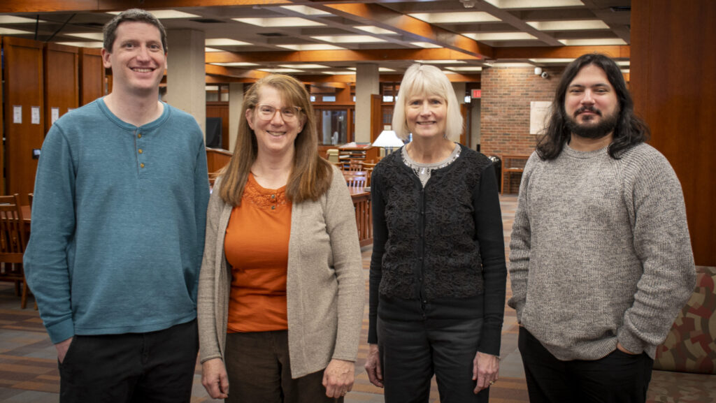 Four members of the Collection Services team stand and smile together inside the library main level.