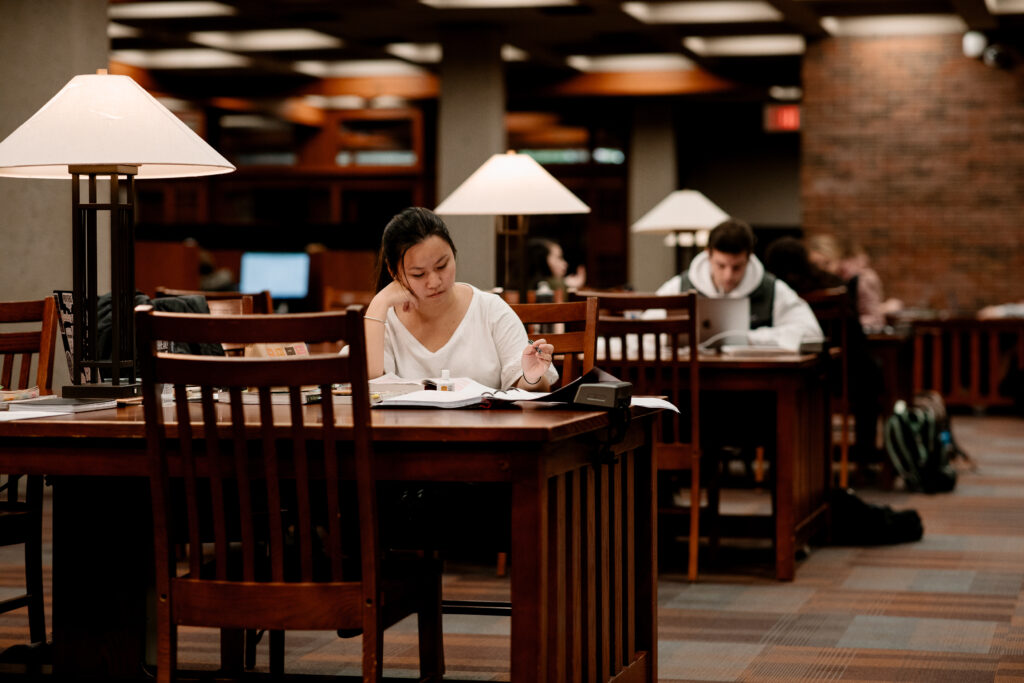 Rows of students studying at lamp-lit tables of the library.