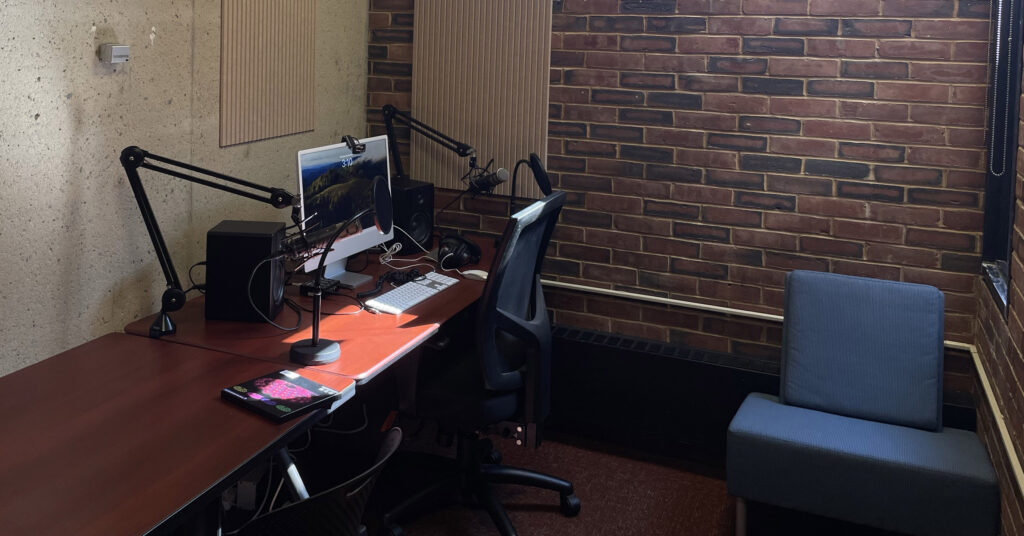 a computer on a desk with two microphones and speakers along with two pop filters in front of the mics. 