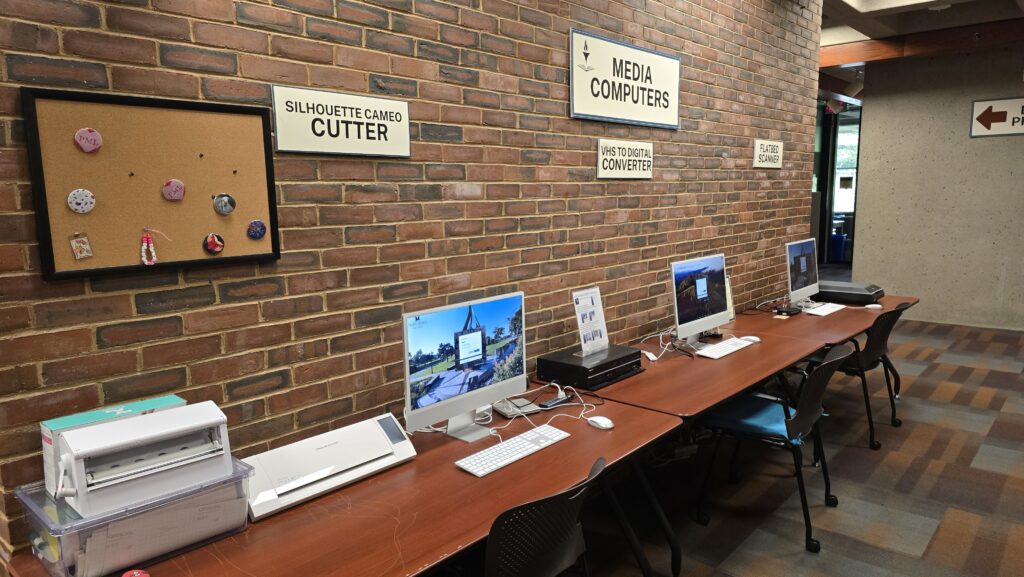 Three Computers on tables against a brick wall with various media equipment 