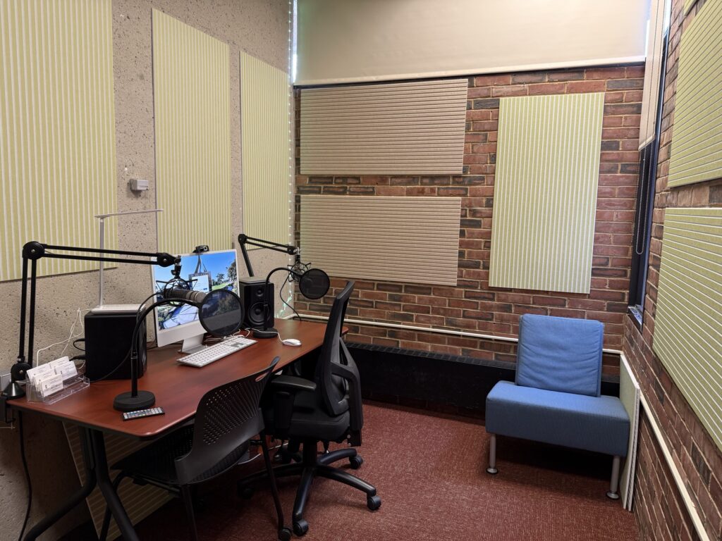 a computer on a desk with two microphones and speakers along with two pop filters in front of the mics.