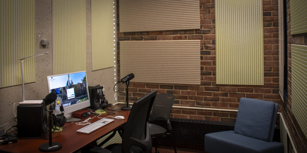 a computer on a desk with two microphones and speakers in a room with sound dampening panels on the walls 