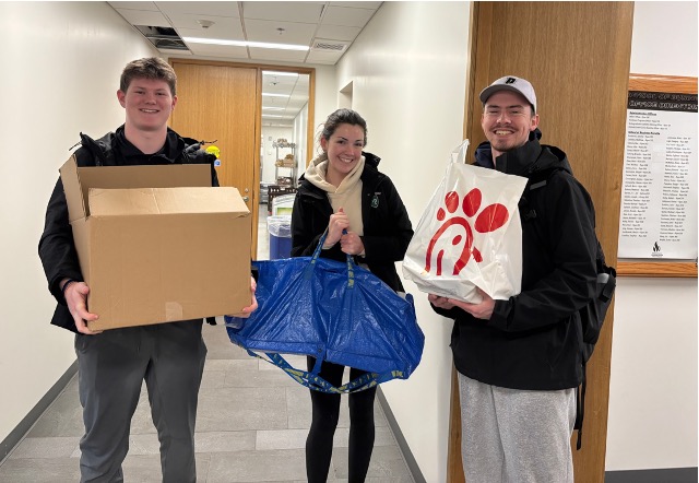 Cailin Fennessy, Sean McCann, and John McDonald stand in a hallway holding bags and boxes of donated books for Providence Books Through Bars