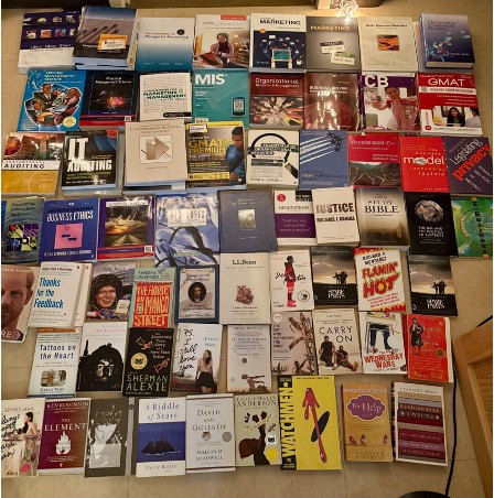 A large collection of donated paperback books is arranged on the floor, including textbooks, novels, and nonfiction titles.